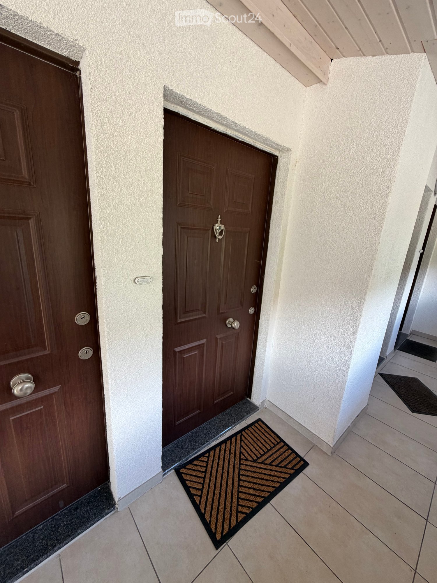 Hallway with two wooden doors, tiled floor, and doormats in front of each door.