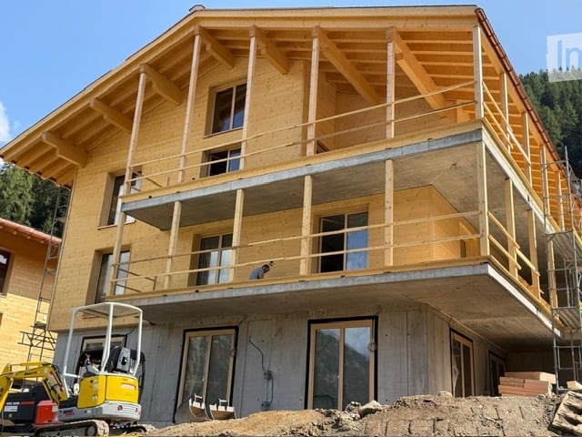 Wooden two-story building under construction with exposed beams, large windows, and a balcony on the upper level.
