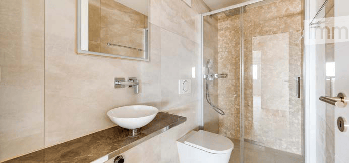 Modern bathroom with a white sink, mirror, toilet, and glass-enclosed shower. Light-colored tiles and sleek fixtures.
