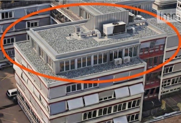 A multi-story building with a flat roof, visible air conditioning units, and surrounding structures.