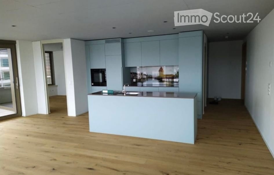 Modern kitchen with light blue cabinets, a central island, and a sleek design. The floor is made of light wood, and the space is bright and open.