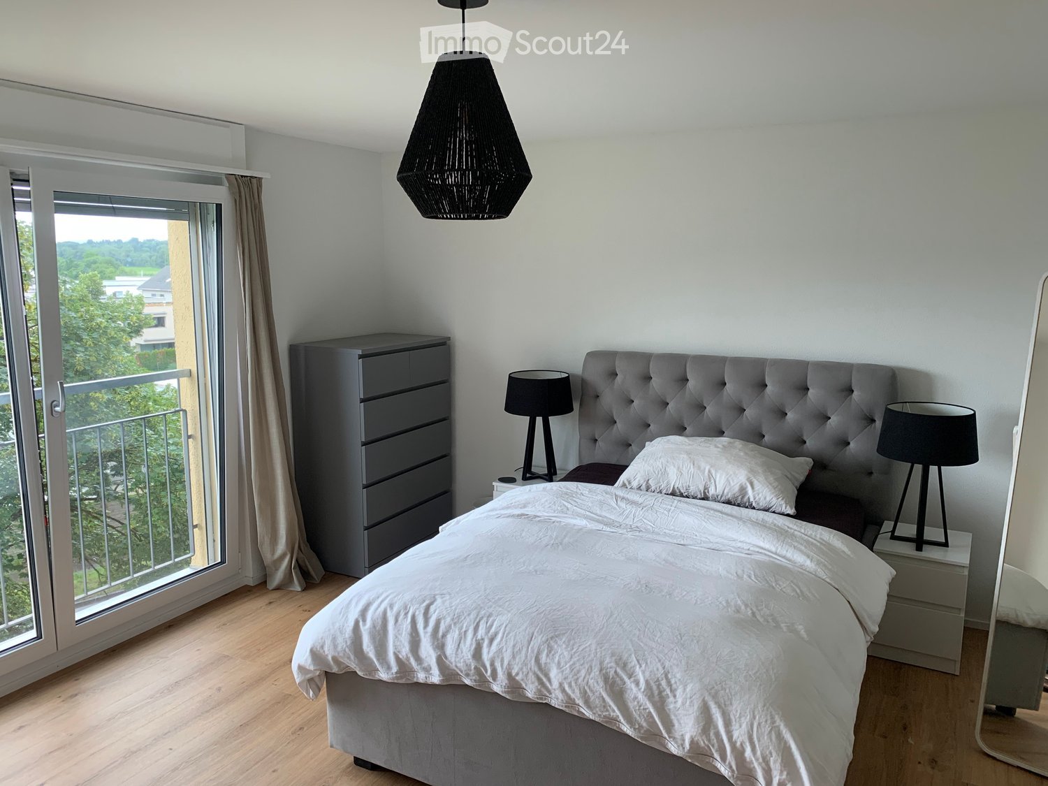 Modern bedroom with a large bed, nightstands, lamps, dresser, and a view of a balcony.