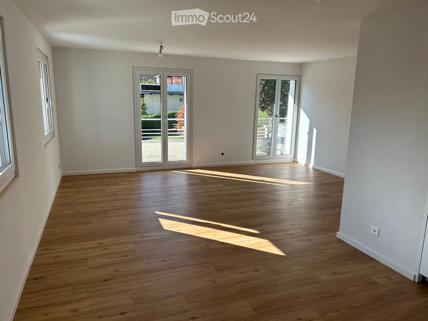 Empty room with wooden flooring, white walls, large windows, and sliding glass doors leading to an outdoor area.