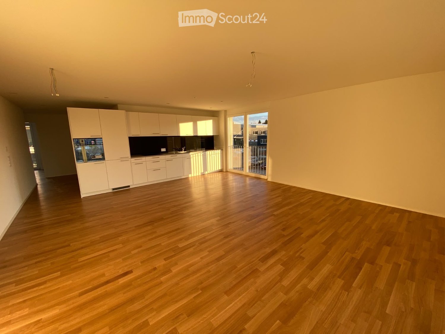Empty room with light wooden flooring, white cabinetry, and large windows letting in natural light.