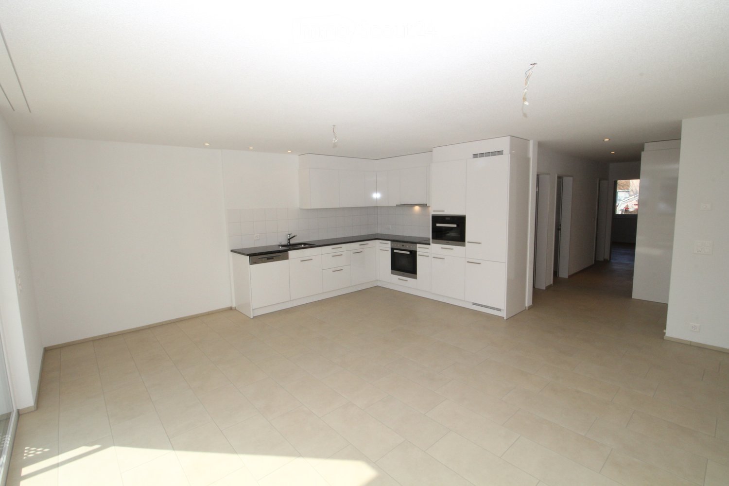 Modern kitchen with white cabinets, black countertops, and built-in appliances including an oven and dishwasher. The space features tiled flooring and ample natural light from a large window.