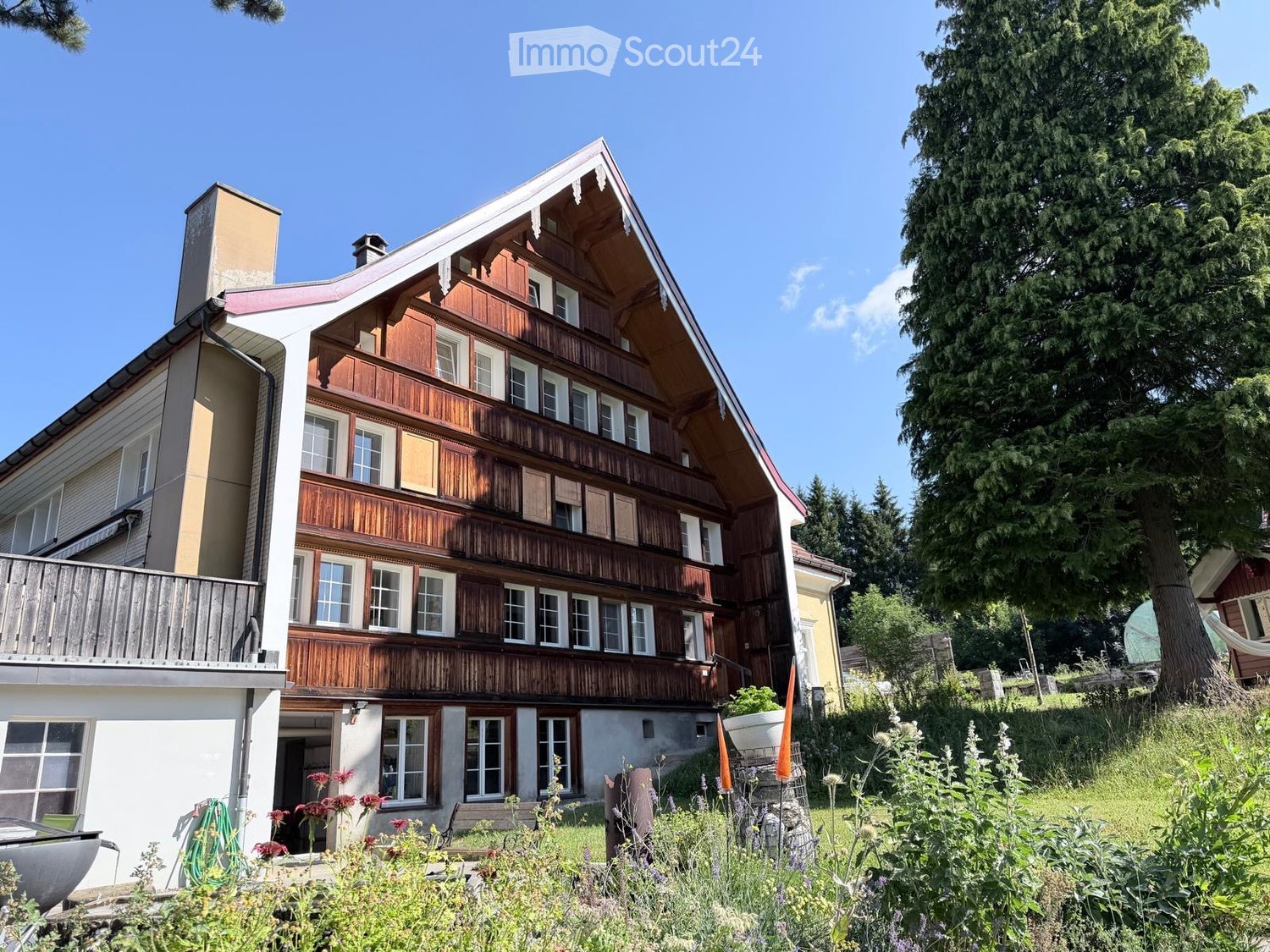 Two-story wooden house with balconies, multiple windows, and a well-maintained garden.
