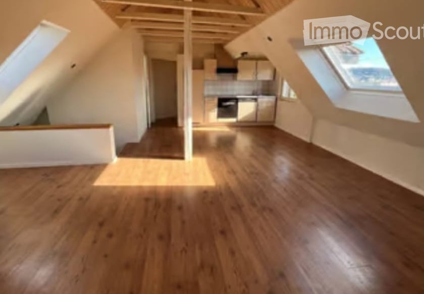 Bright, empty attic space with wooden flooring, exposed wooden beams, and built-in kitchen cabinets. Large skylights provide natural light.