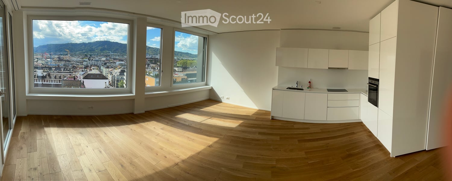 Modern kitchen with white cabinets, wooden flooring, and large windows offering a scenic city view.