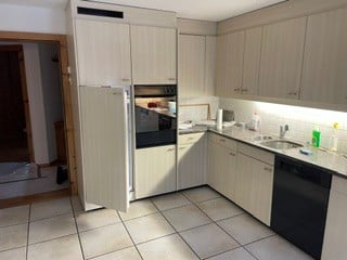 Modern kitchen with light wood cabinets, stainless steel appliances, and a tiled floor.
