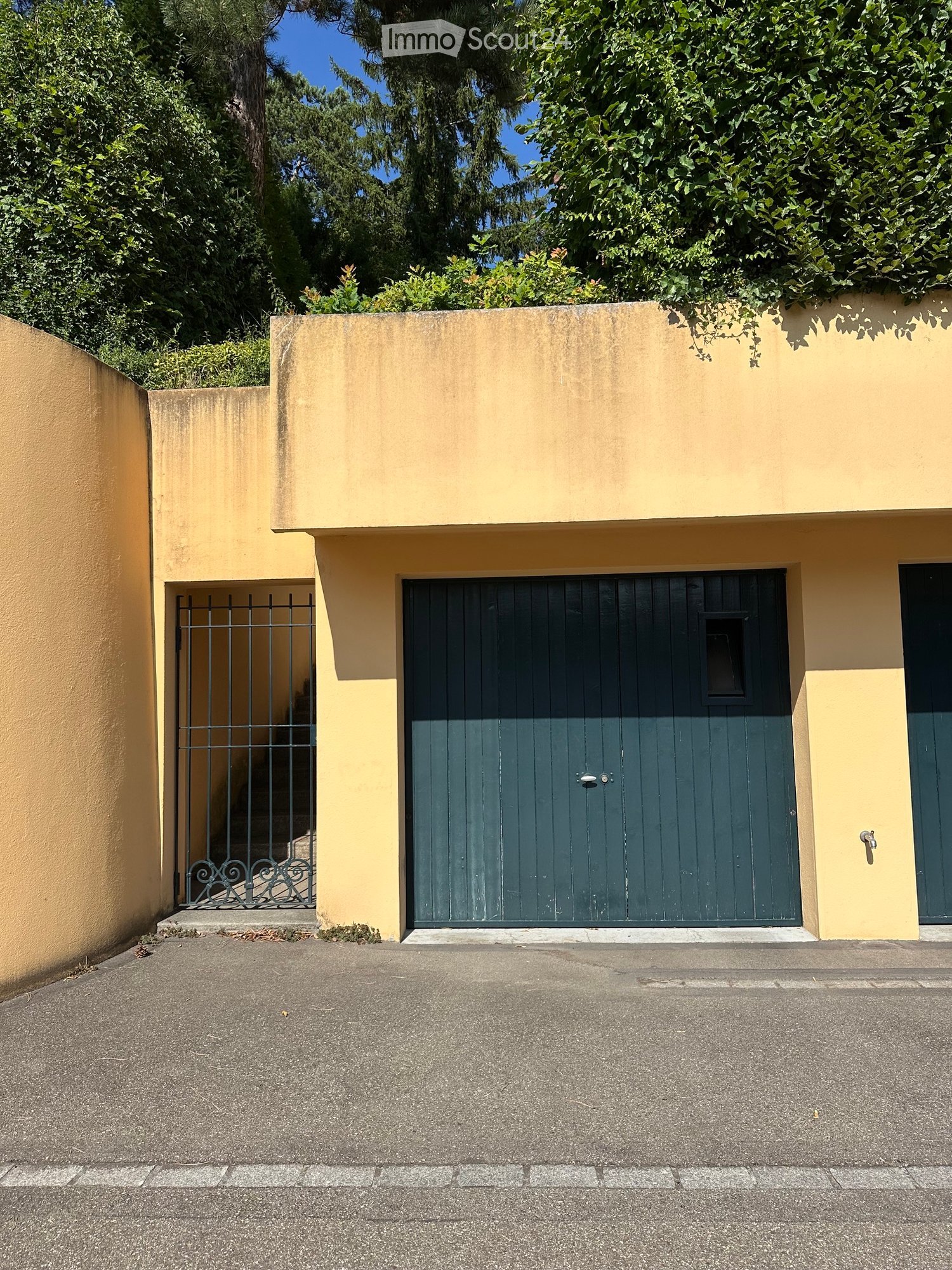 A two-story building with a yellow facade, green garage door, and metal gate entrance.