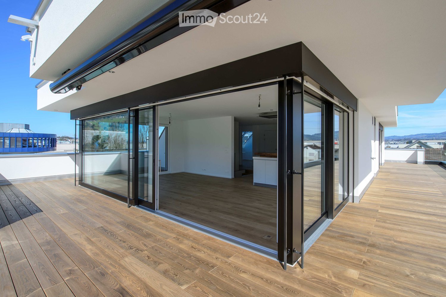 Modern balcony with wooden flooring, large glass sliding doors, and a view of the city and mountains.