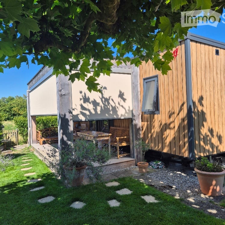 A wooden cabin with a covered patio area, outdoor furniture, and potted plants in a garden setting.