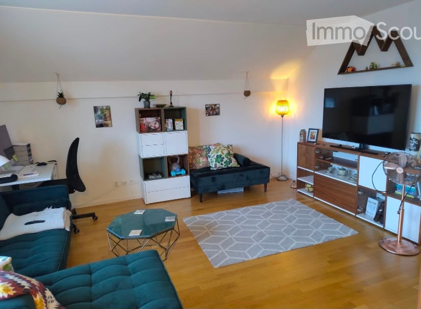 A modern living room with wooden flooring, a grey sofa, a coffee table, a shelf, a fan, a lamp, and a screen.