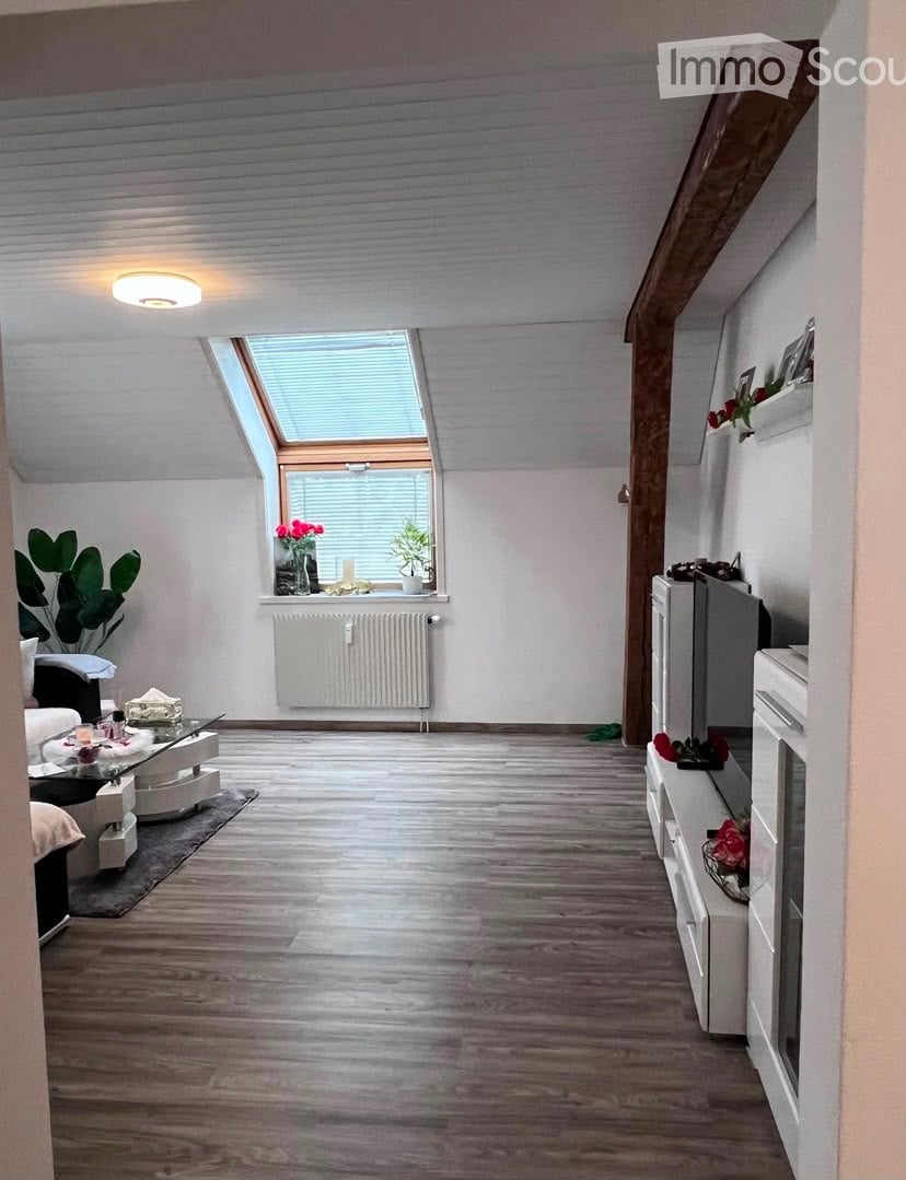 Modern living room with wooden flooring, white walls, skylight window, sofa, coffee table, TV stand, and decorative plants.