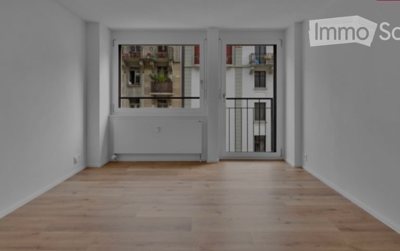 Empty room with wooden flooring, large window with balcony access, radiator, and white walls.