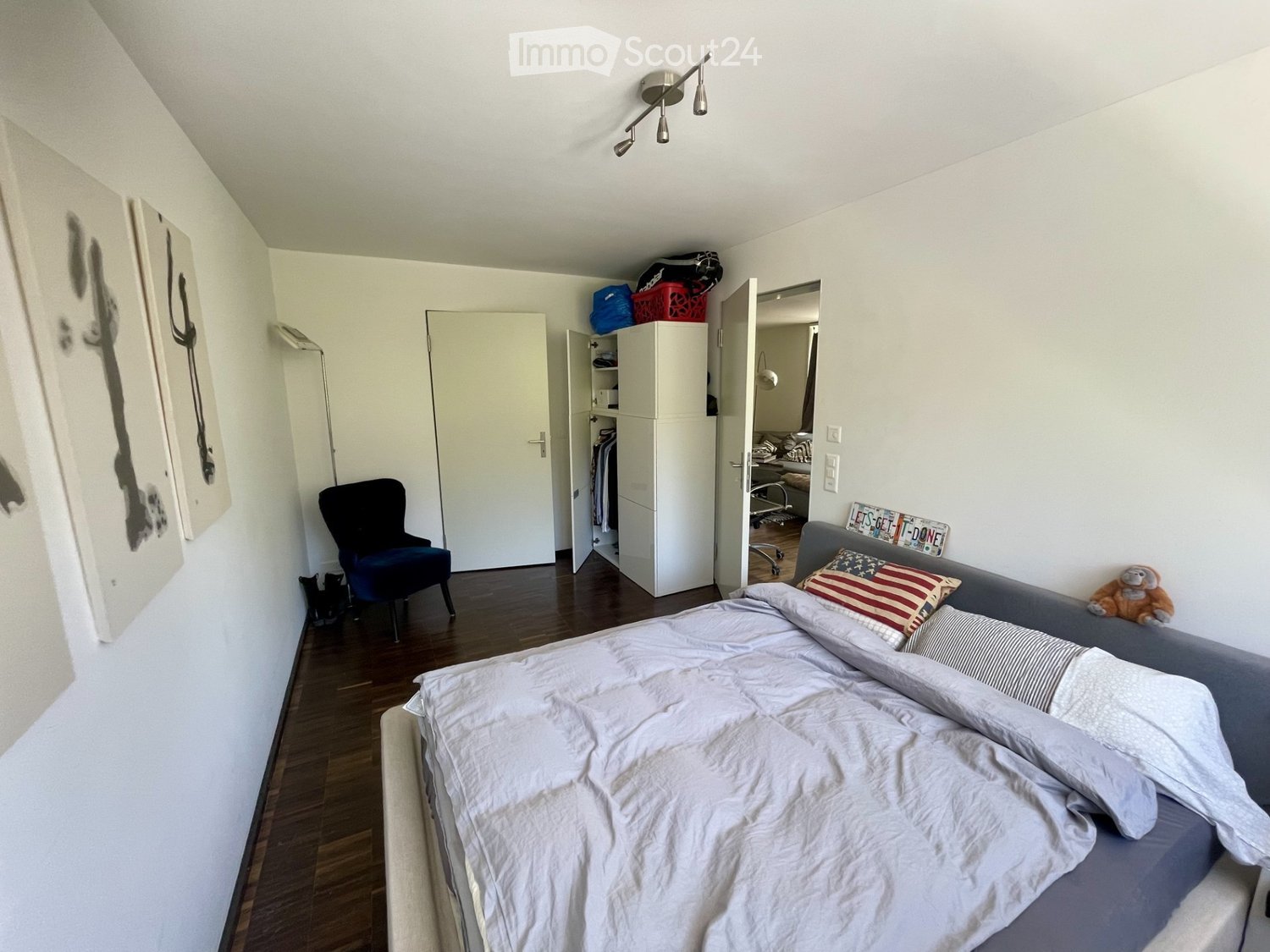 Cozy bedroom with a bed, sofa, chair, wardrobe, and a small cat. The room features wooden flooring and white walls.