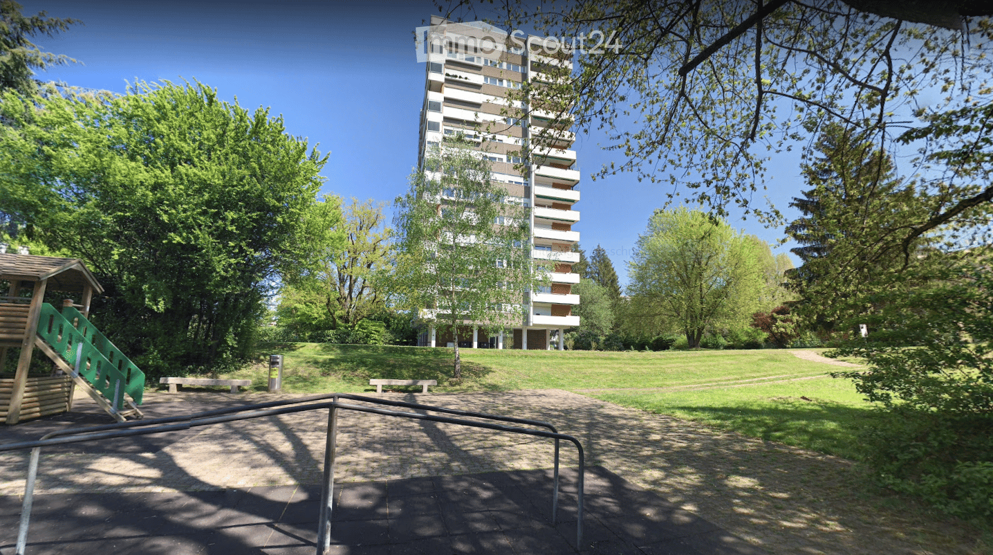 A park area with a playground, benches, and a multi-story residential building in the background.
