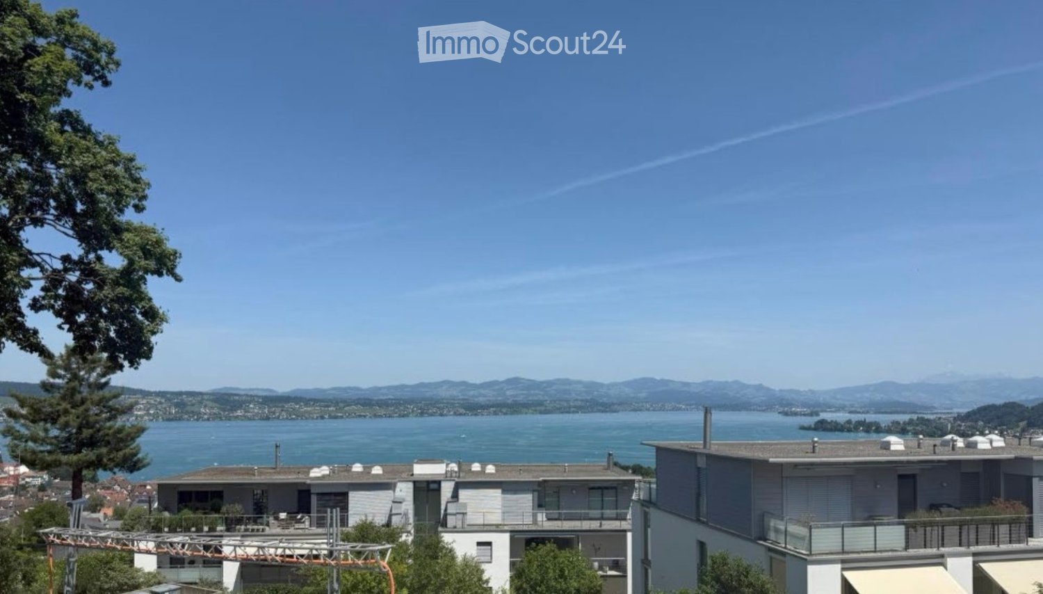 Modern multi-story building with balconies overlooking a scenic lake and distant mountains.