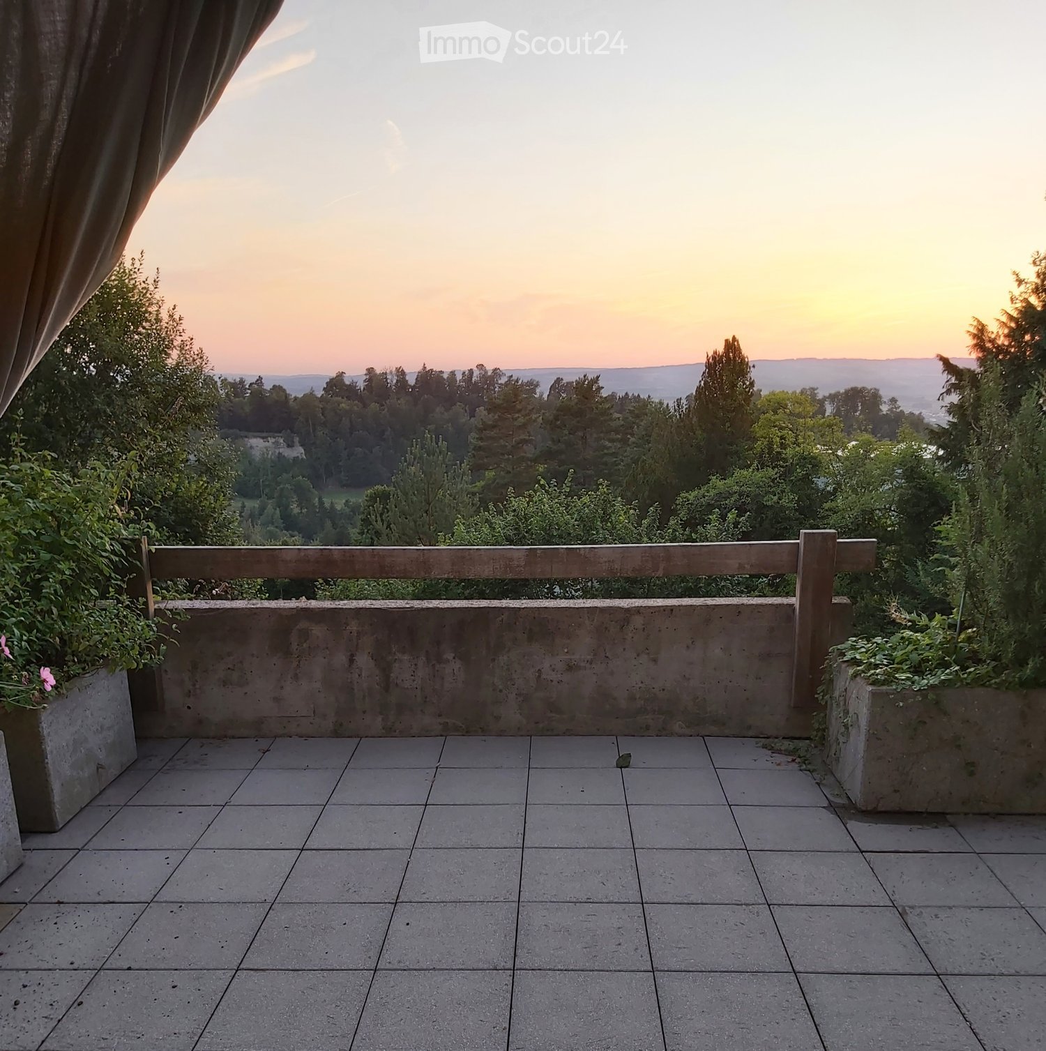 Balcony with tiled floor, wooden railing, and scenic view of a valley at sunset.