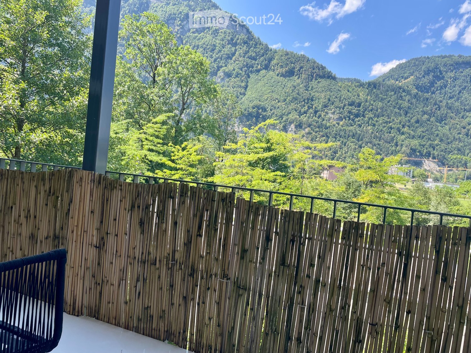 Balcony with wooden privacy screen, overlooking a lush green valley and mountains under a clear blue sky.