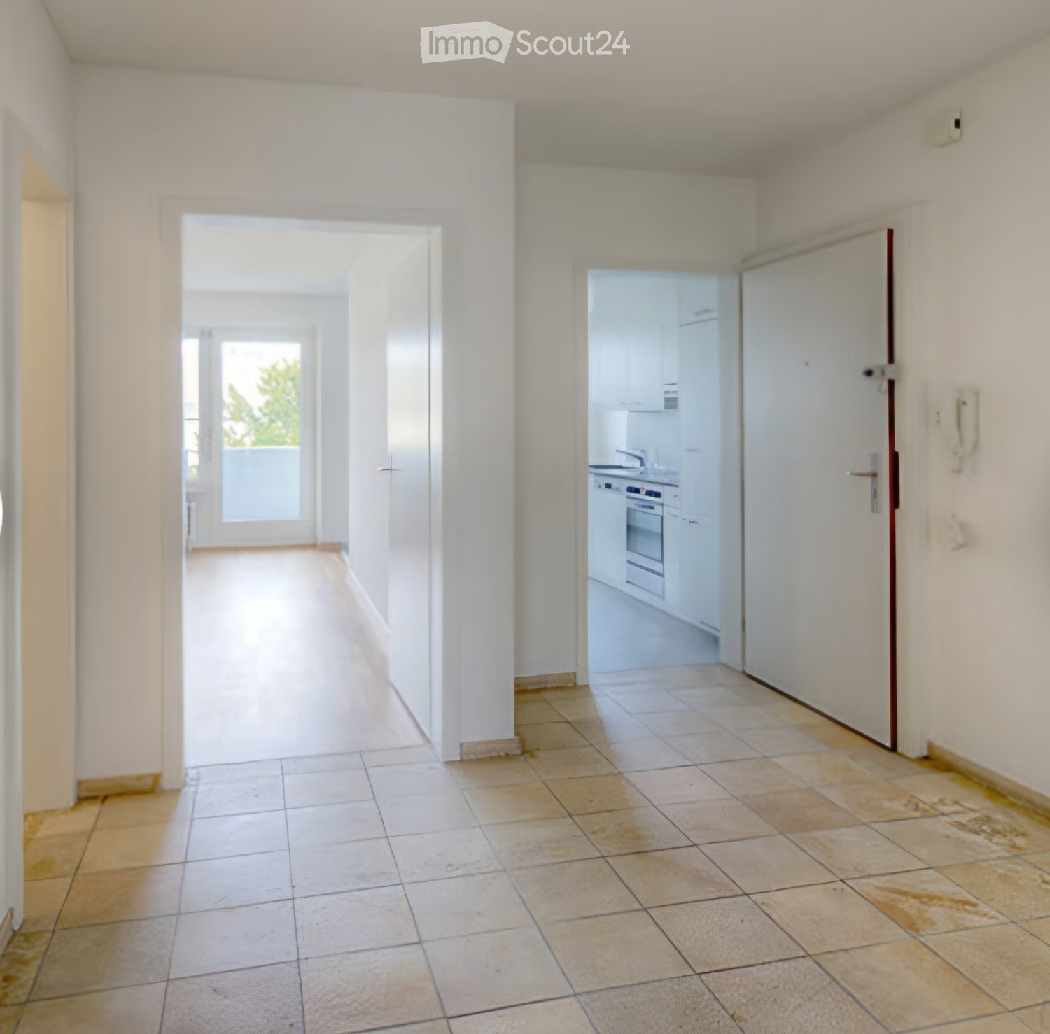 Empty hallway with tiled floor, white walls, and doors leading to other rooms, including a kitchen area visible through an open door.