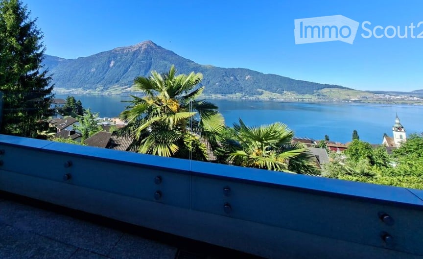 Balcony with a scenic view of a lake and mountains, surrounded by palm trees and greenery.