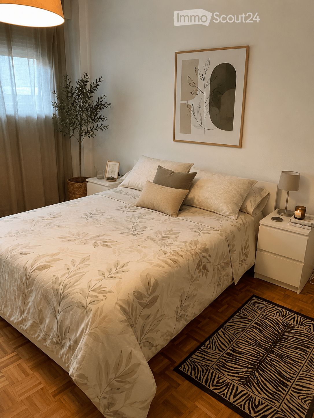 A modern bedroom with a large bed, patterned bedding, nightstands, lamps, a framed picture, and a plant in the corner.