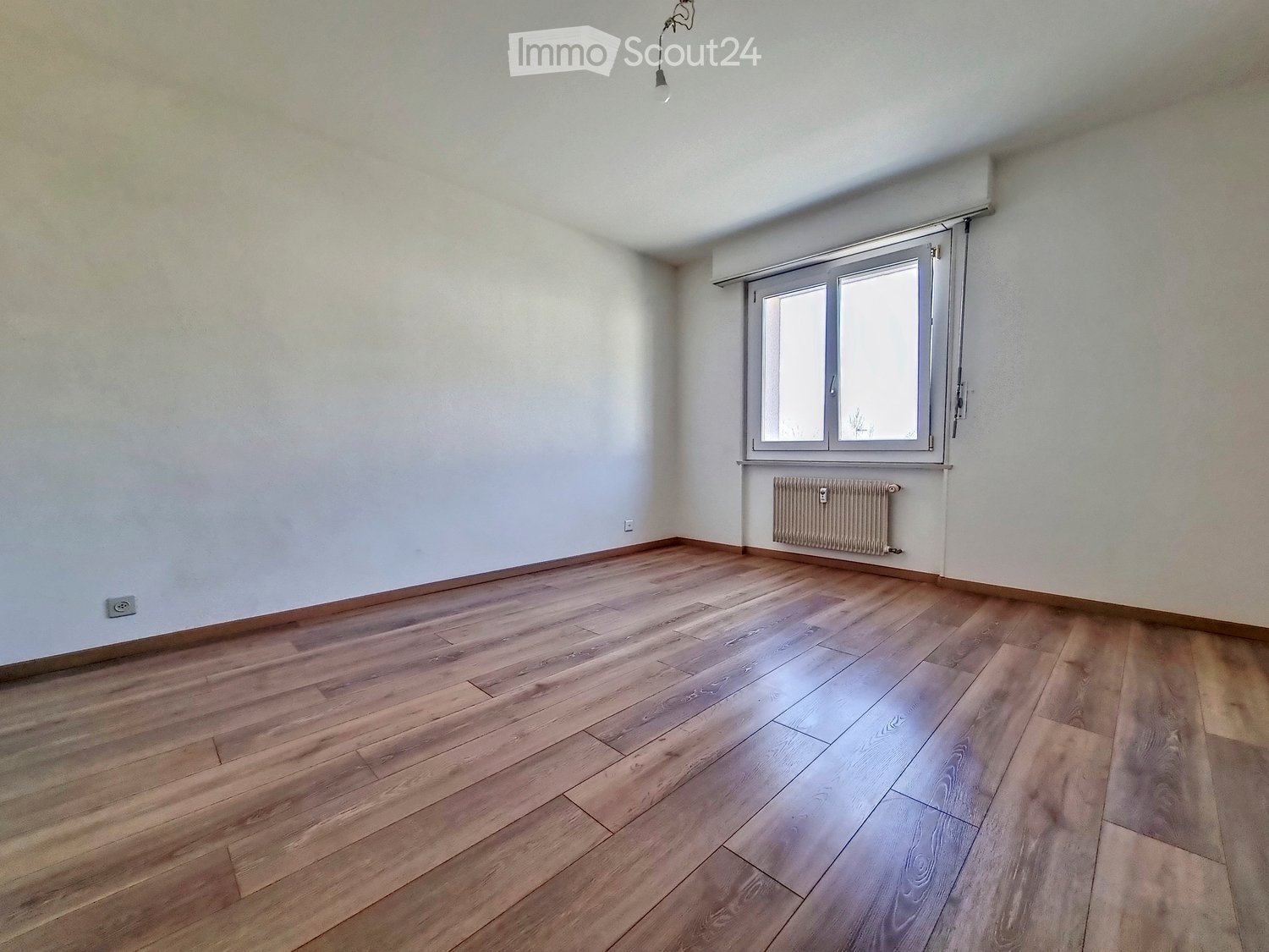 Empty room with wooden flooring, white walls, a window with blinds, and a radiator under the window.