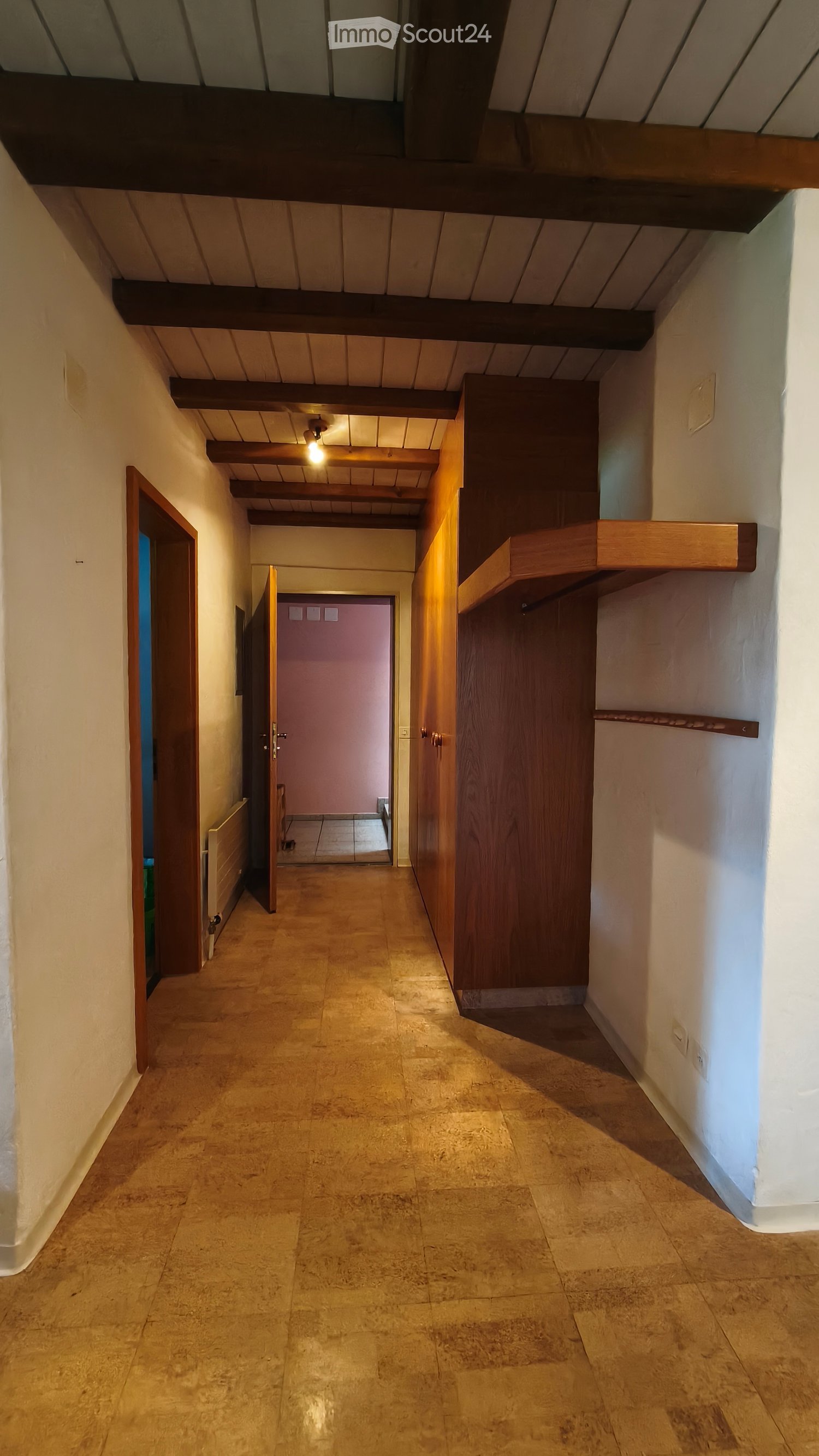 A long, narrow hallway with wooden beams on the ceiling, tiled floor, and several doors leading to different rooms.
