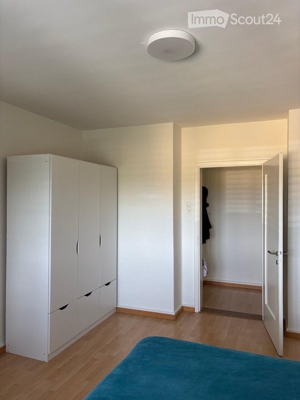A modern, minimalistic bedroom with a blue bedspread, white wardrobe, and wooden flooring.