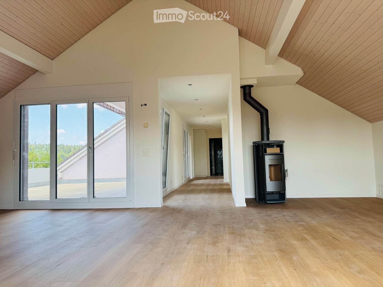 Empty room with wooden flooring, white walls, and a modern fireplace. Large sliding glass doors lead to a balcony area.