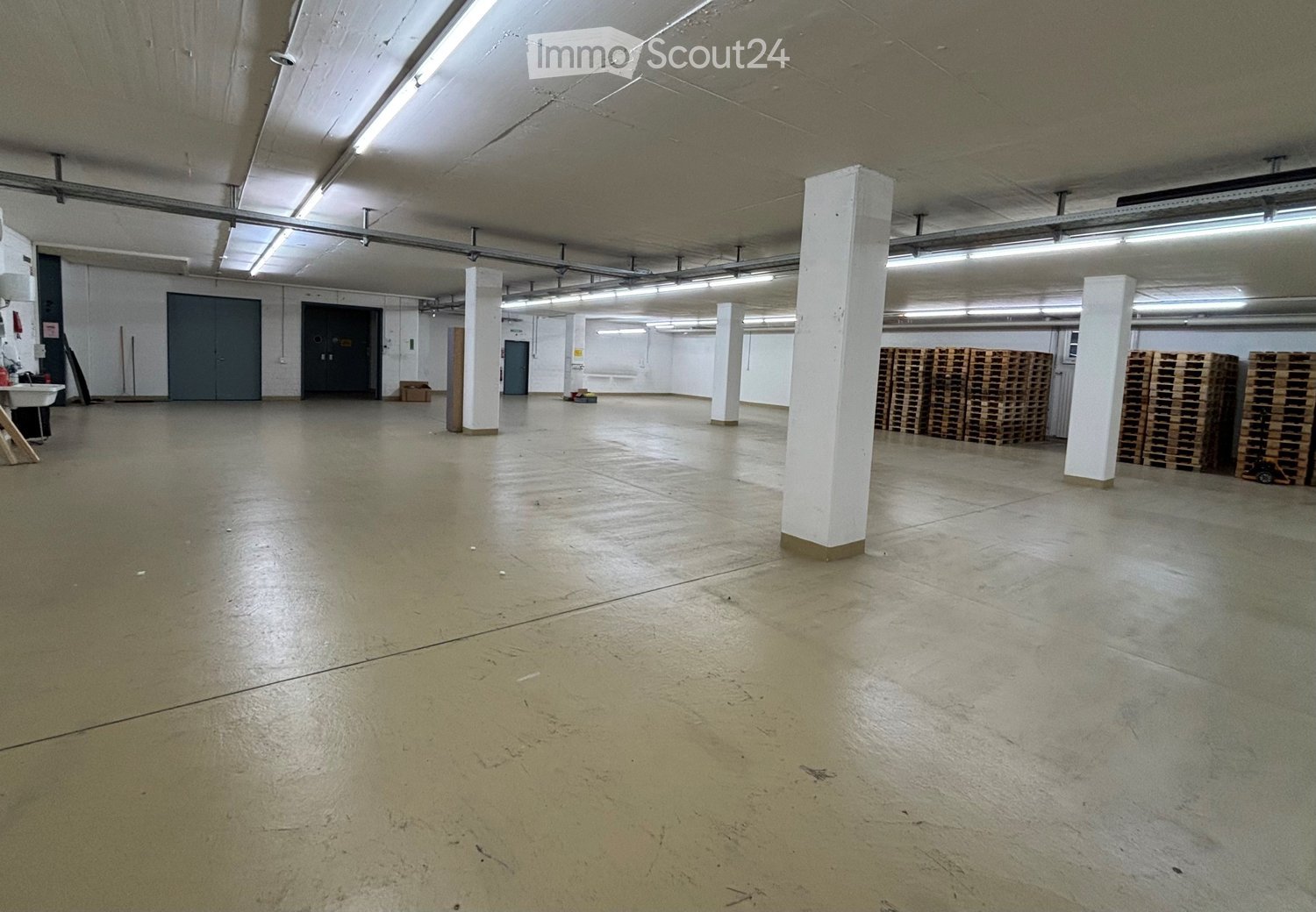 A large, empty garage with concrete floors, metal beams, large windows, and stacks of wooden pallets.