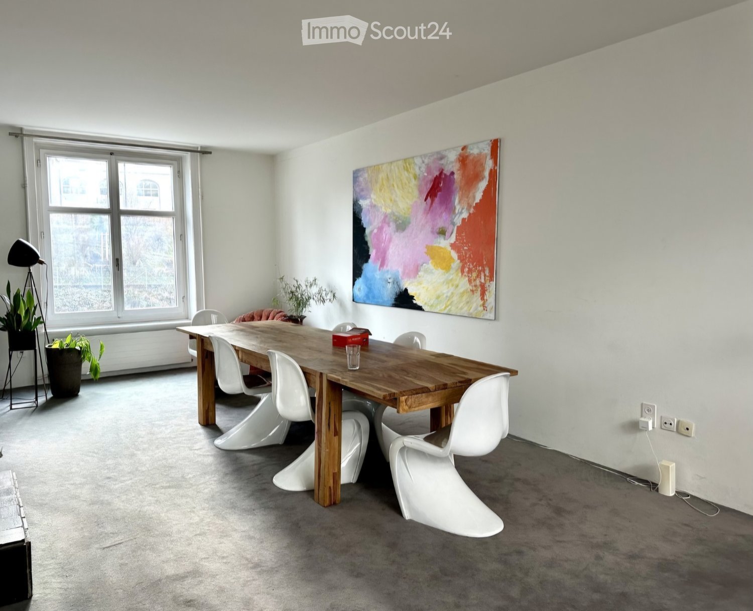 Modern dining area with a wooden table, white chairs, a colorful abstract painting, and a floor lamp near the window.