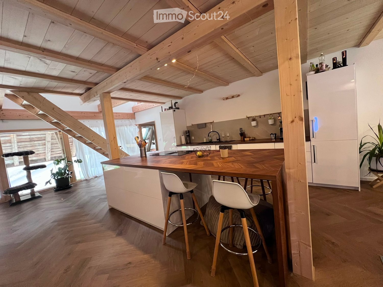 Modern kitchen with wooden island, white stools, stainless steel appliances, and exposed wooden beams on the ceiling.