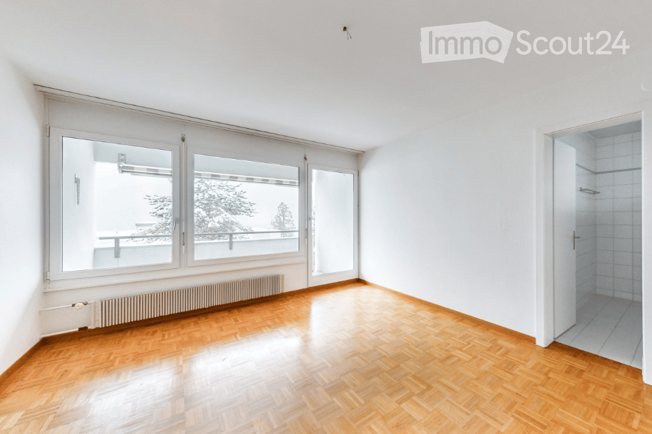 Empty room with wooden flooring, large windows, radiator, and a view of a balcony area.