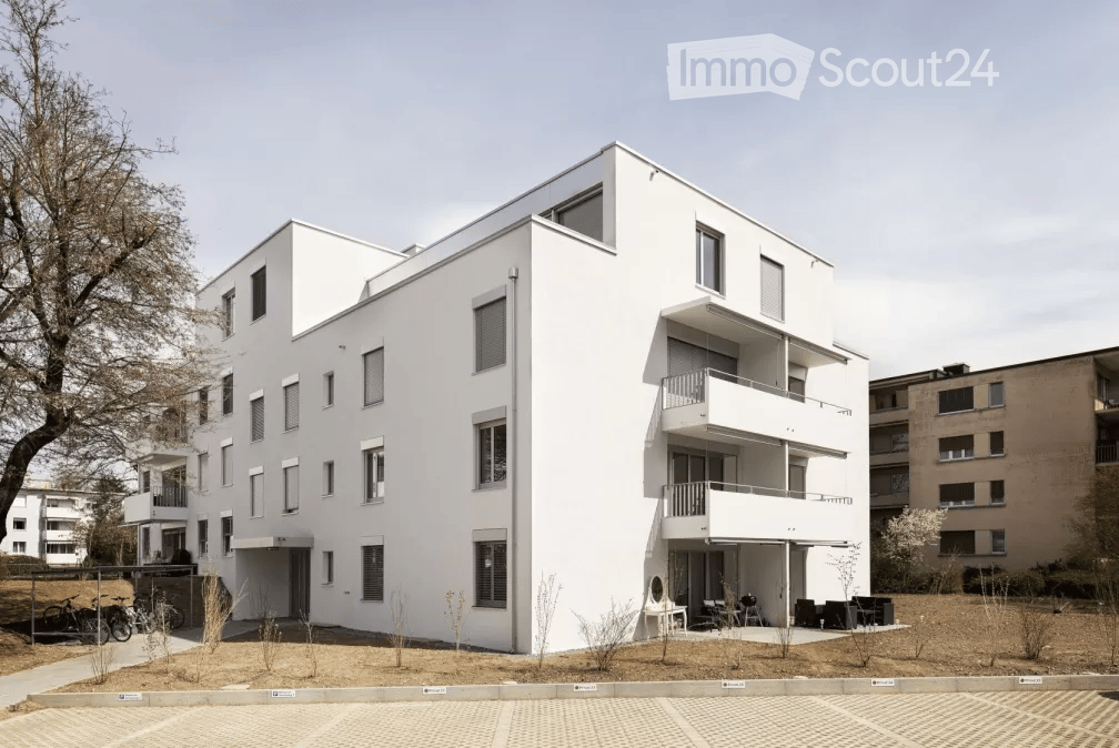 Modern white multi-story residential building with balconies and large windows.