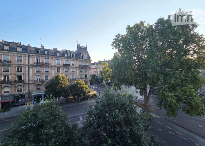 Balcony overlooking a city street with classic European buildings, trees, and a clear sky.