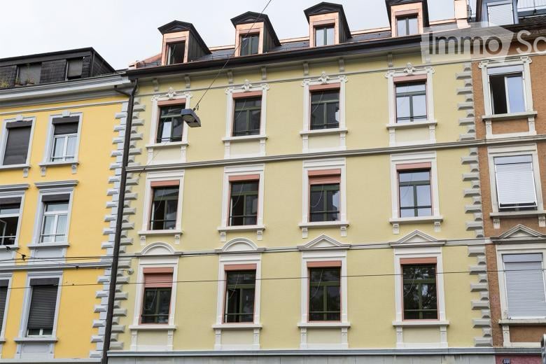 Multi-story building with yellow facade, white trim around windows, and decorative architectural details. Windows have shutters, and the roof features dormer windows.