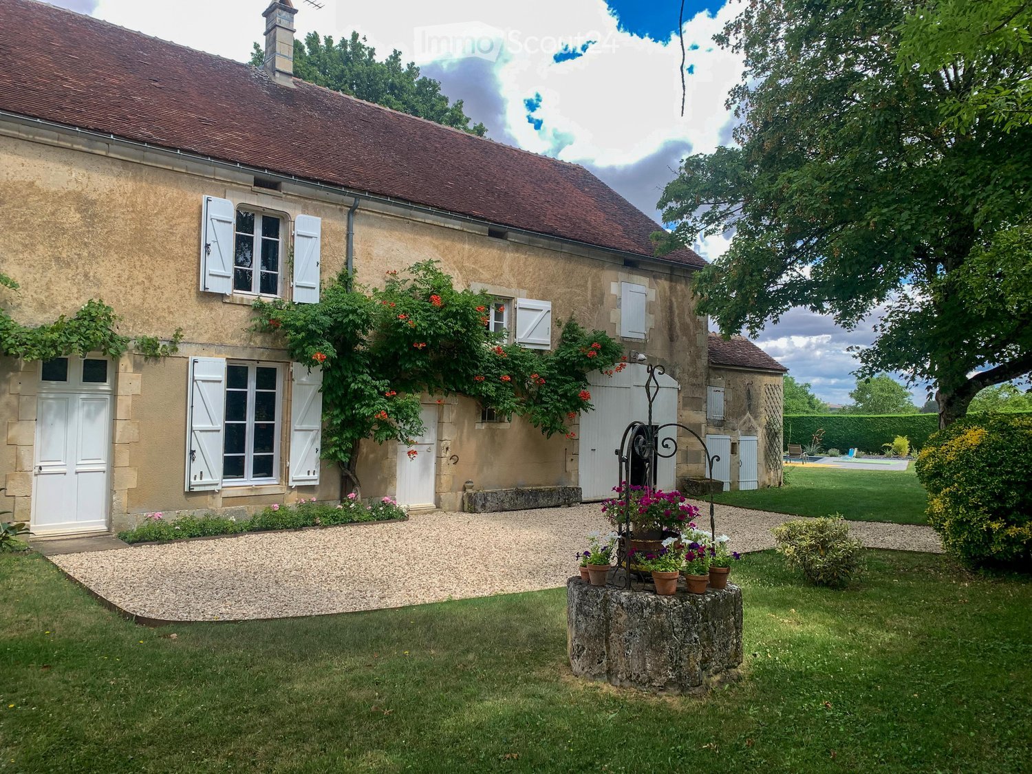 A charming stone house with a red-tiled roof, surrounded by a well-maintained garden and a gravel driveway.