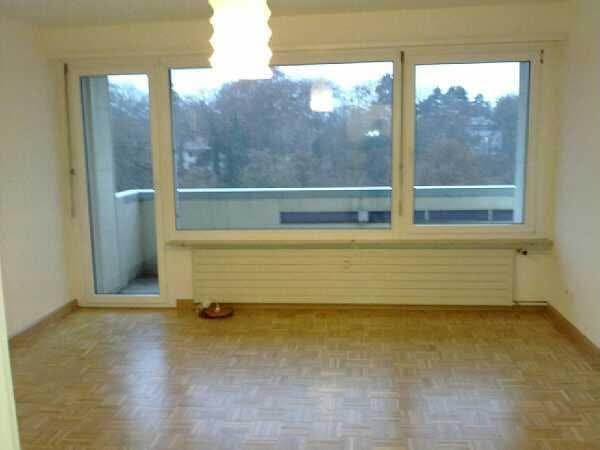 Empty room with wooden flooring, large windows, and a balcony access door. No furniture or equipment present.