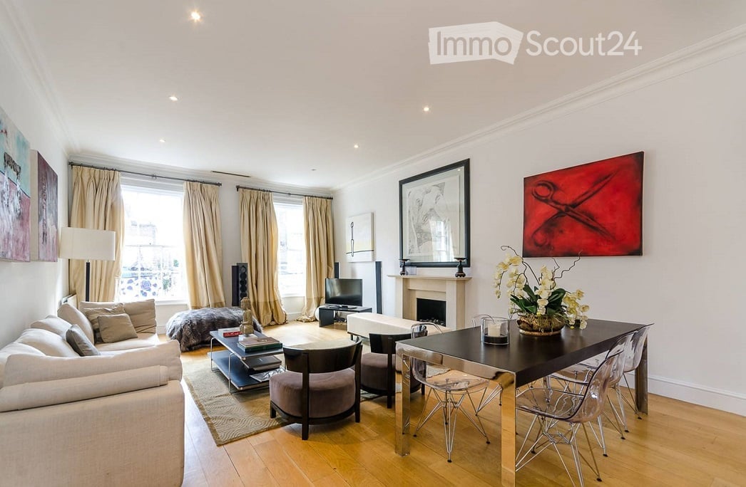 Modern living room with large windows, white walls, a fireplace, a sofa, coffee table, armchairs, a TV, and a dining table with chairs.