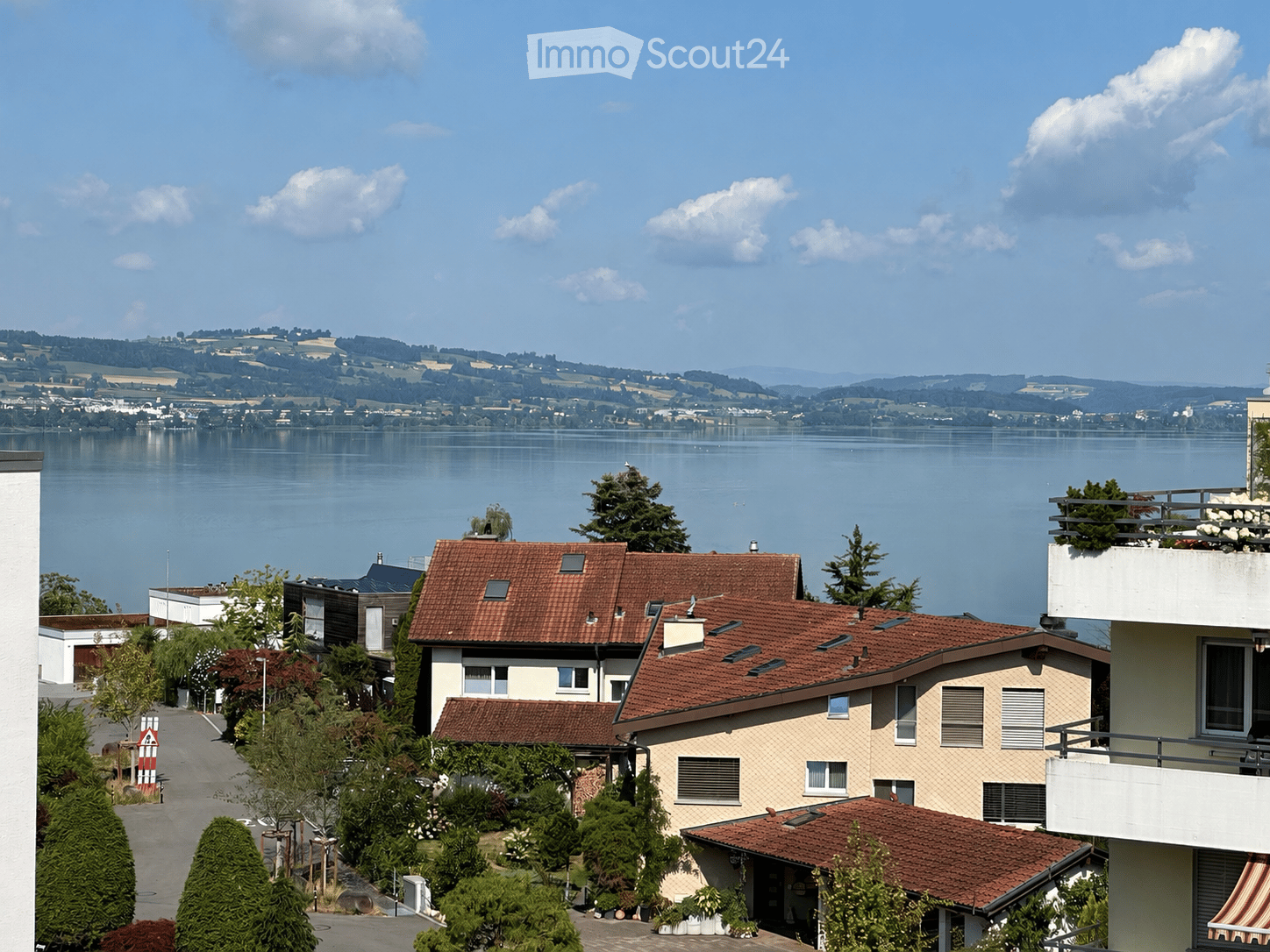 Residential houses with red-tiled roofs and balconies overlooking a serene lake and distant hills.