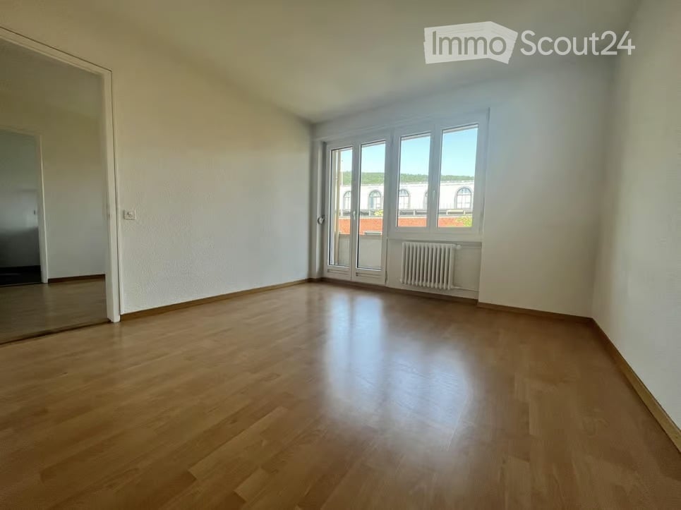 Empty room with wooden flooring, white walls, large windows, and a radiator. No furniture or equipment present.