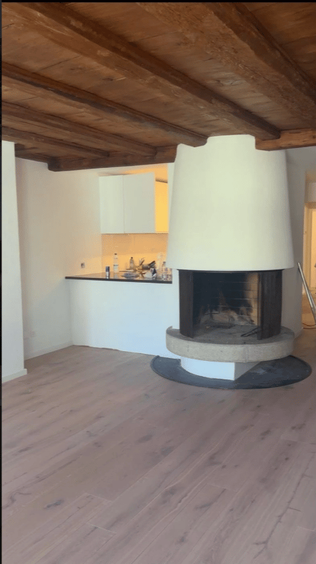 Open-plan living and kitchen area with exposed wooden ceiling beams, a modern fireplace, and a sleek kitchen counter with cabinets.