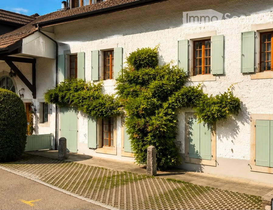 A charming white house with green shutters and a well-maintained garden, featuring neatly trimmed bushes and a cobblestone pathway.