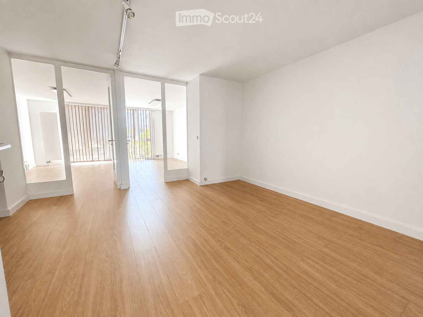 Empty room with light wooden flooring and white walls, featuring large sliding glass doors leading to another space.
