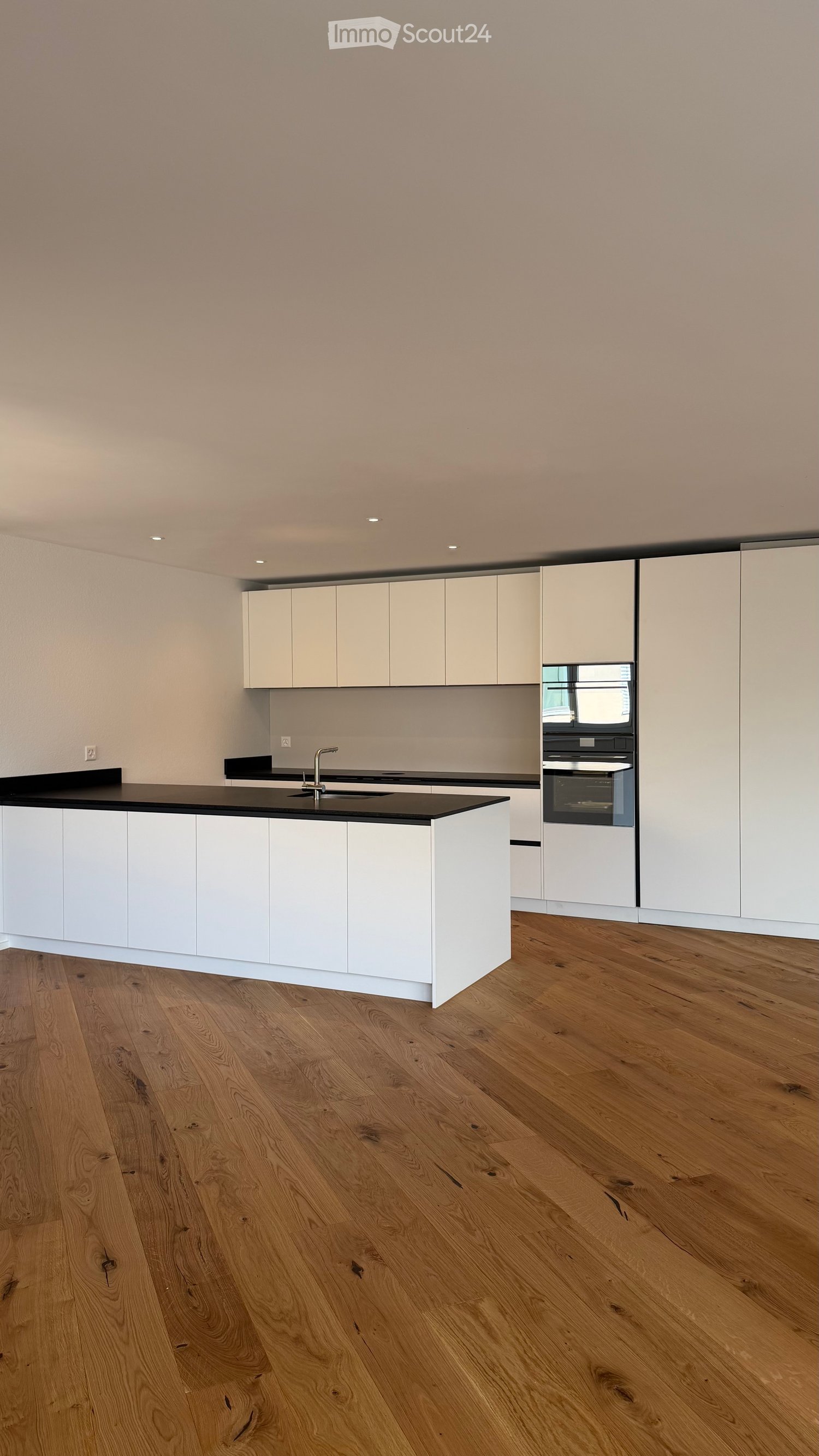 Modern kitchen with white cabinets, black countertop, and wooden flooring.