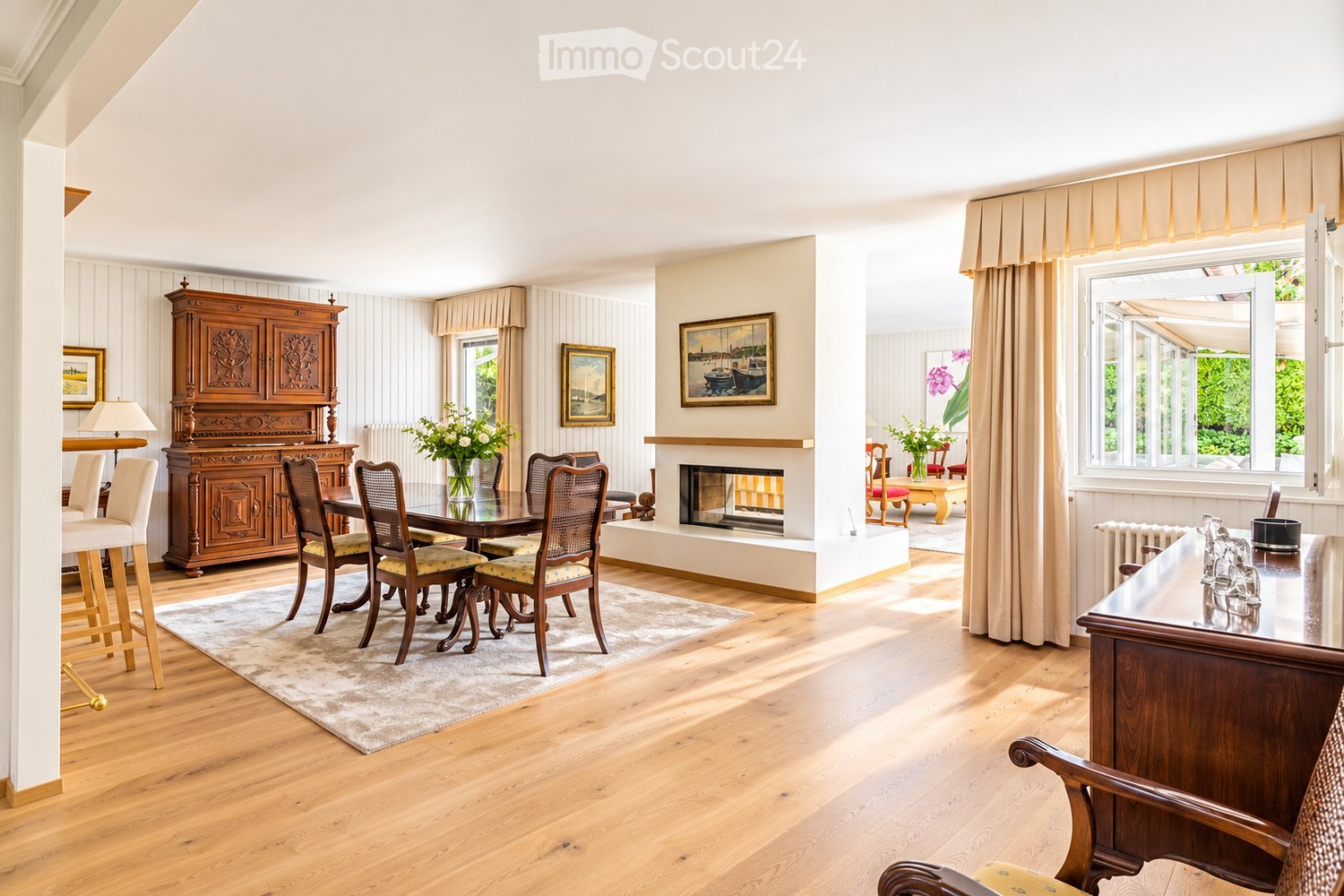 Elegant dining area with wooden flooring, a fireplace, a large dining table with chairs, a wooden cabinet, and decorative vases.