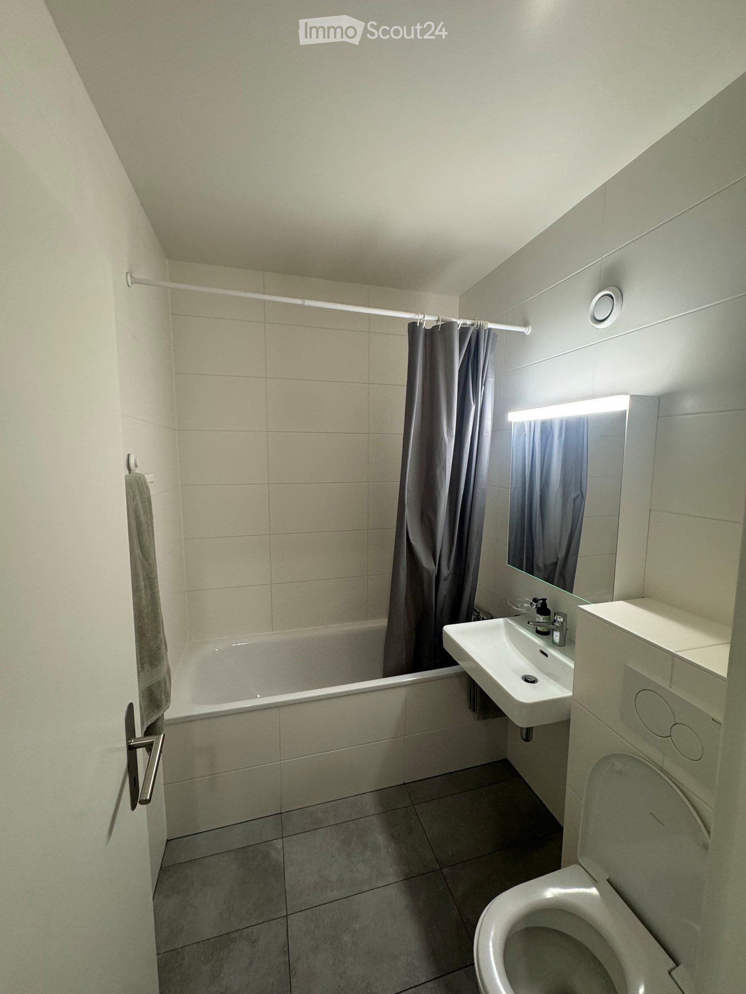 Modern bathroom with a bathtub, sink, toilet, mirror, and shower curtain. Light-colored tiles and a built-in vanity with a mirror.
