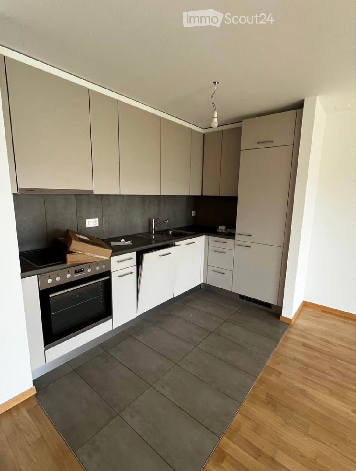 Modern kitchen with white cabinets, grey tiles, and a wooden floor. Features an oven, sink, and faucet.